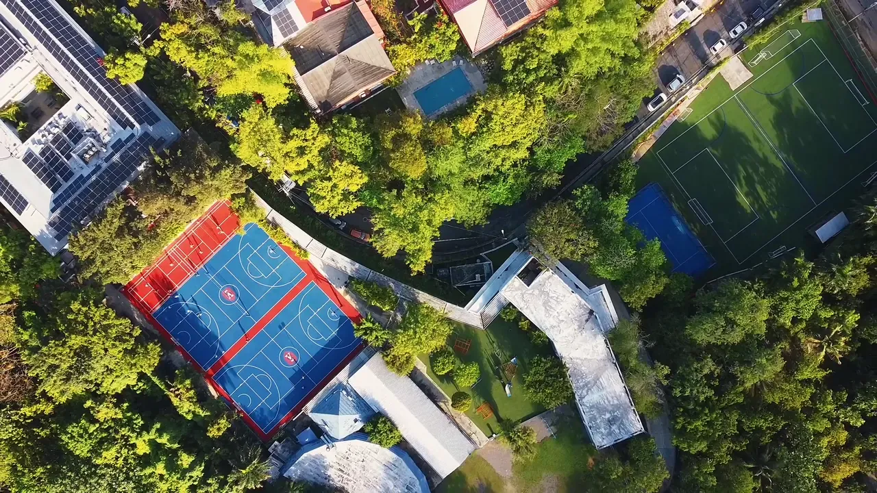 Vista aérea del American School of Santo Domingo con sus canchas de baloncesto y fútbol rodeadas de árboles, en Cerros de Arroyo Hondo