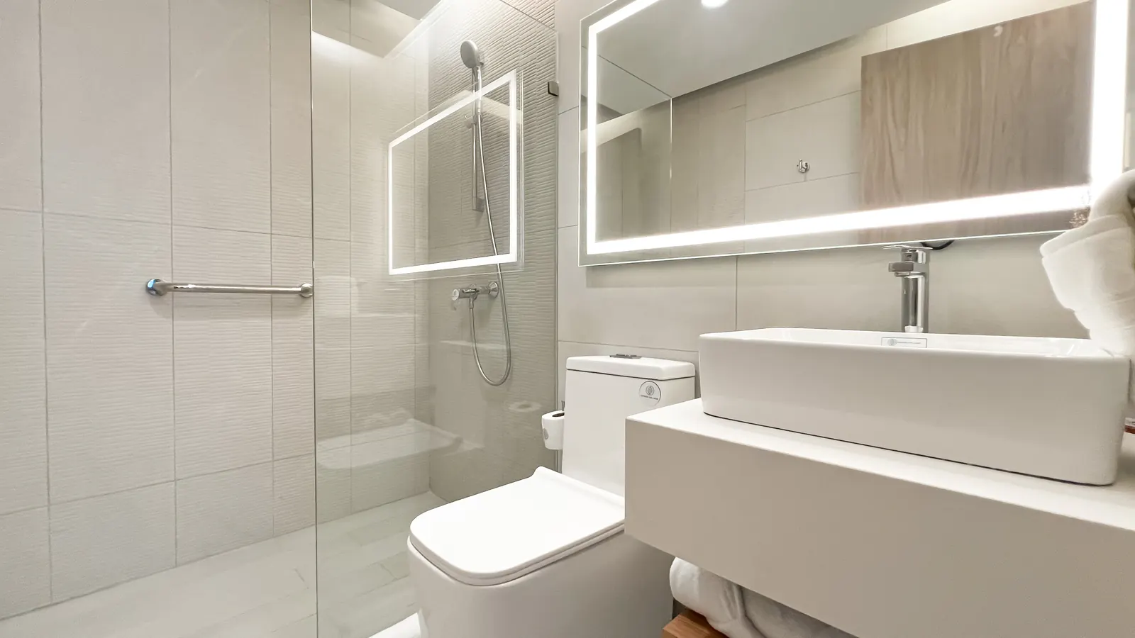 Baño con mampara de vidrio y espejo iluminado del apartamento modelo de Cruise On Land