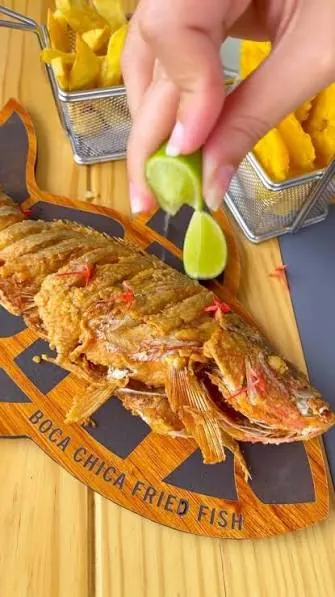 Pescado frito entero con limón y papas fritas sobre una tabla grabada con el nombre Boca Chica Fried Fish