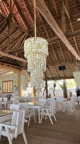 Salón de Bocana Beach con una gran lámpara de conchas, techo de guano y piso de madera