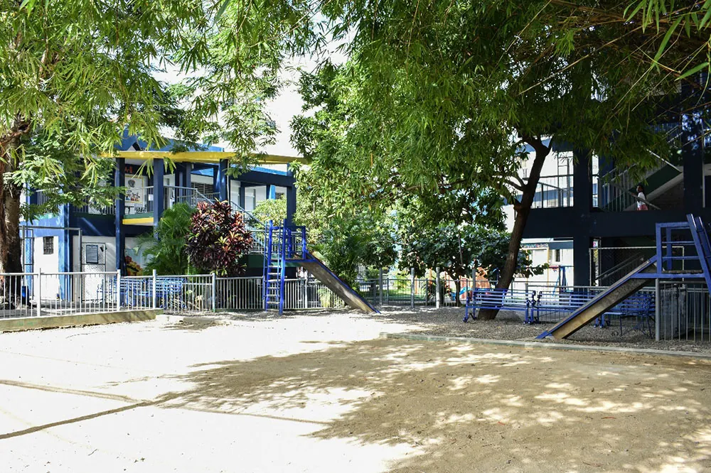 Área de juegos con toboganes bajo los árboles en el Colegio Padres y Maestros, Arroyo Hondo