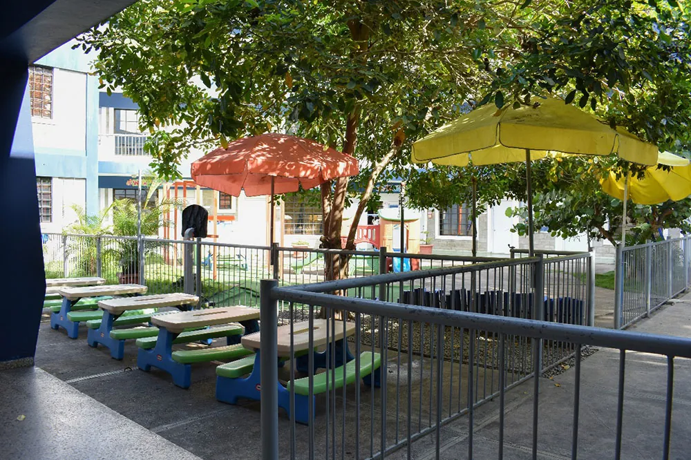 Mesas de colores con sombrillas en un patio del Colegio Padres y Maestros, Arroyo Hondo