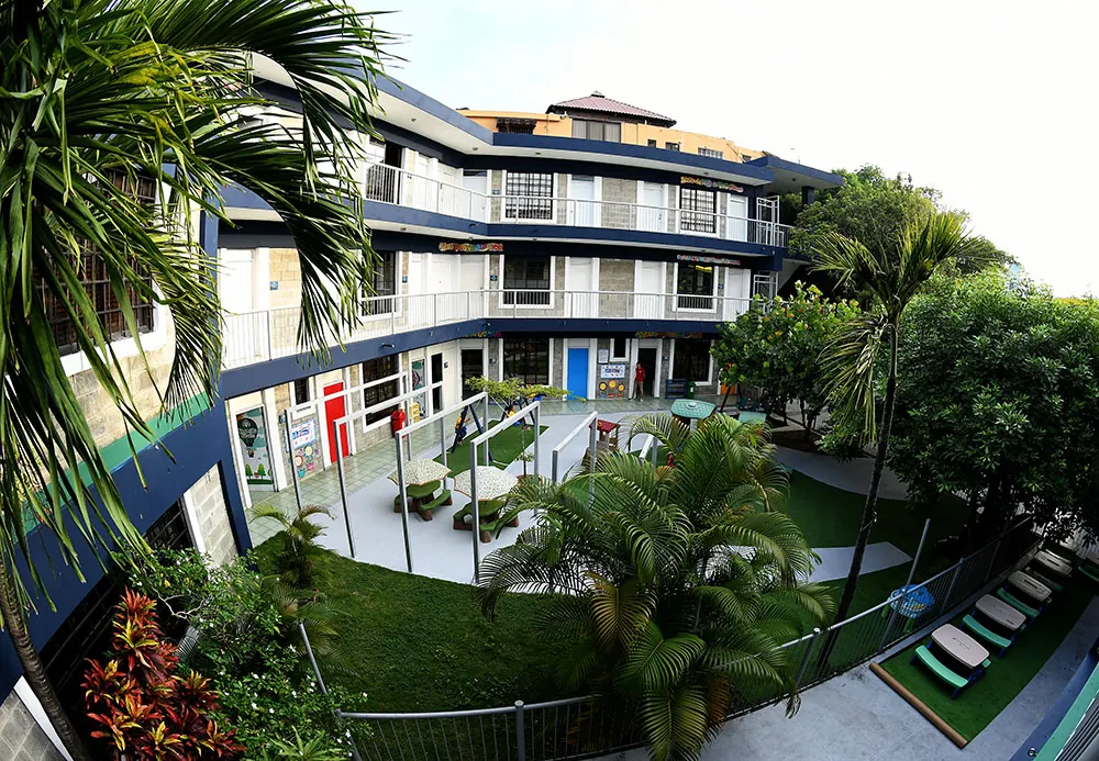 Patio central del Colegio Padres y Maestros en Arroyo Hondo II, con el edificio de tres niveles, palmas y mesas de picnic