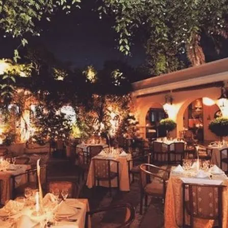 Patio de La Briciola de noche, con mesas iluminadas bajo los árboles en la Zona Colonial