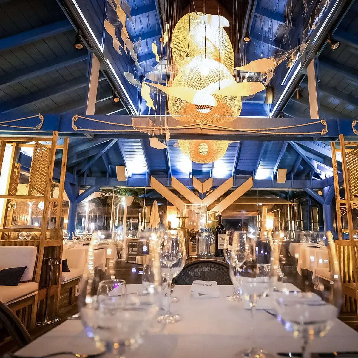 Salón de La Proa Bistro Marino con techo azul, lámparas en forma de pez y mesas puestas