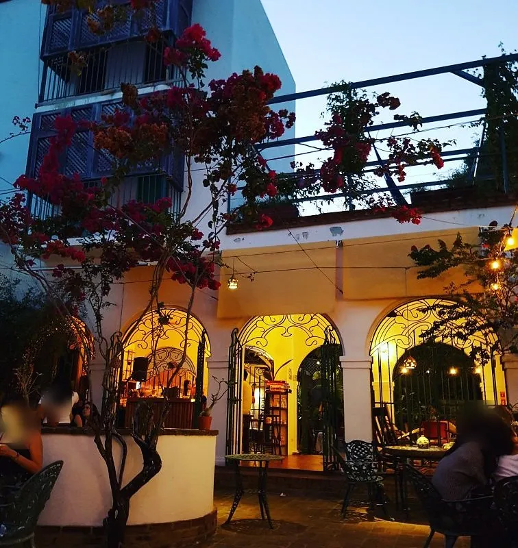 Patio de Mamey Librería Café al anochecer, con arcos iluminados, buganvilias y mesas de hierro