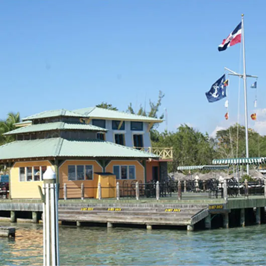 Restaurante de la Marina Zar Par en un edificio de madera amarillo junto al muelle, con banderas, en Andrés