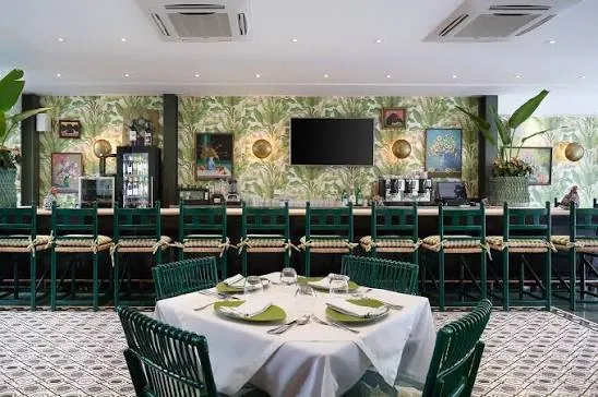 Barra del Mesón de Bari con sillas verdes y papel tapiz de hojas tropicales