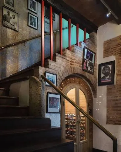 Escalera del Mesón de Bari con fotos de artistas en la pared y una cava de vinos con puerta en arco