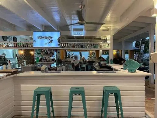 Barra de Mie by Sporting Club con taburetes verdes, botellas y un pez decorativo
