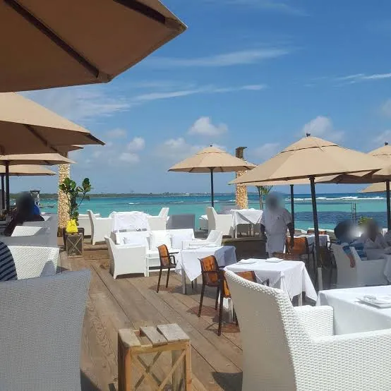 Terraza de Neptunos con sombrillas, mesas de mantel blanco y el mar turquesa de Boca Chica al fondo