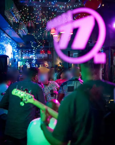Banda tocando en vivo en Parada 77, con el neón rosado del número 77 y el público al fondo, Zona Colonial