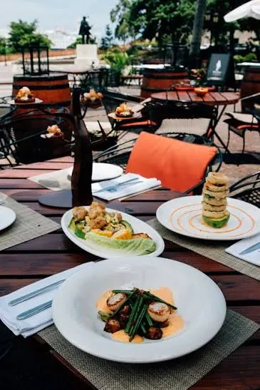 Platos servidos en una mesa de la terraza de Pat'e Palo, con barriles de madera y la plaza al fondo
