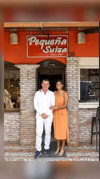 Una pareja frente a la fachada del restaurante Pequeña Suiza en la calle Duarte de Boca Chica, con el letrero «Since 1983»