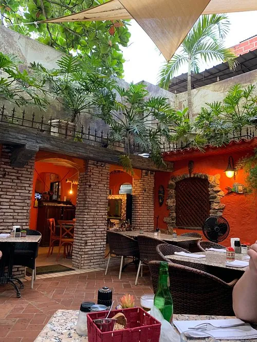 Patio interior de Pequeña Suiza con paredes naranjas, columnas de ladrillo, plantas y mesas