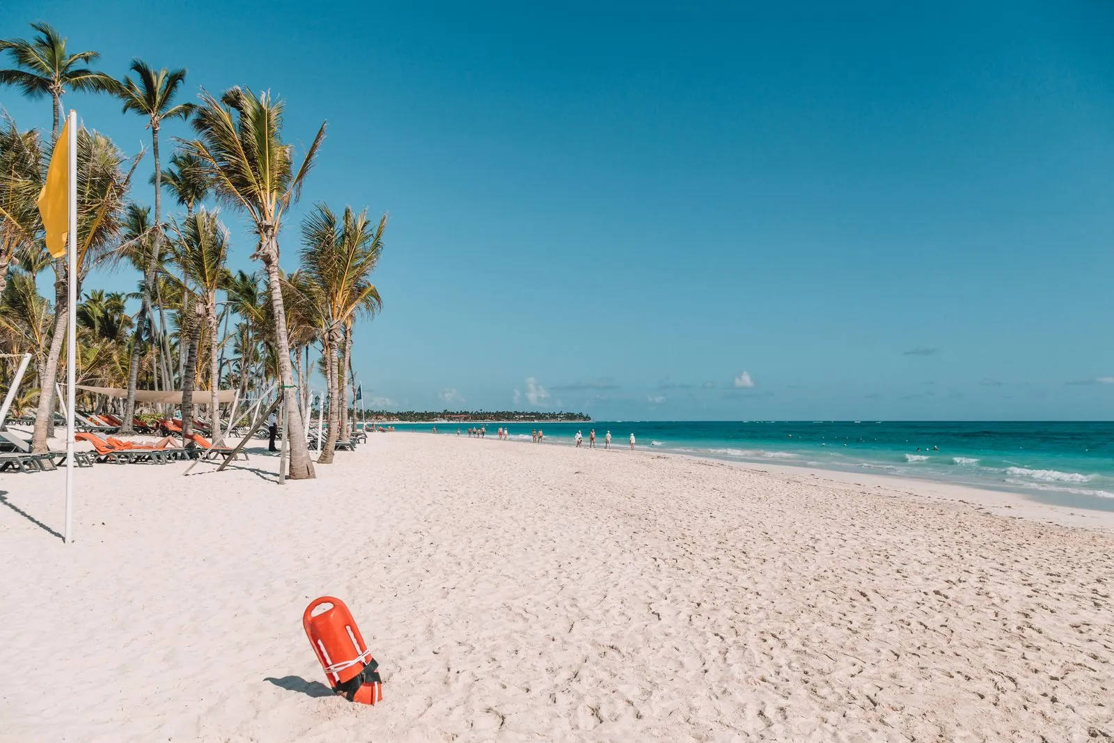 Playa de arena blanca con palmeras y agua turquesa en Punta Cana, República Dominicana, con una boya roja de salvavidas en la arena