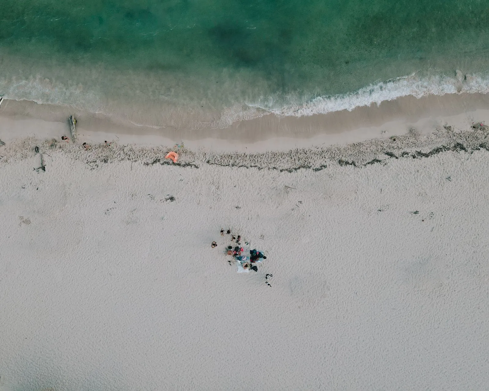 Vista aérea de la arena blanca y el agua turquesa de la playa de Juan Dolio, con un grupo de personas sentadas en la orilla