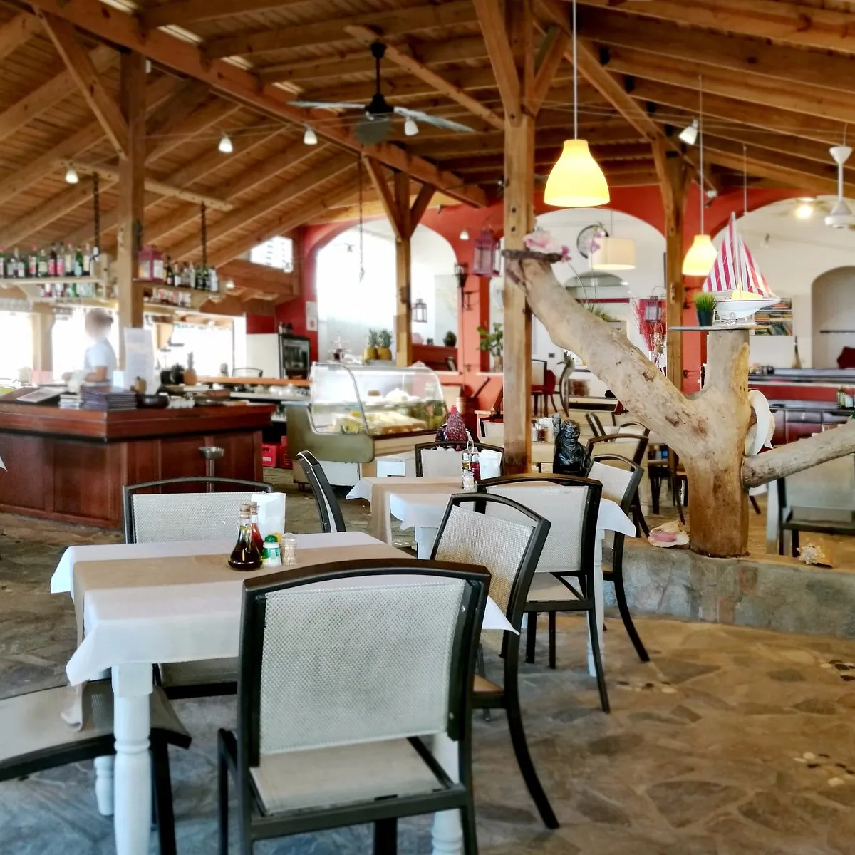 Salón de El Puerco Rosado con techo de madera, lámparas colgantes y un tronco de árbol decorativo