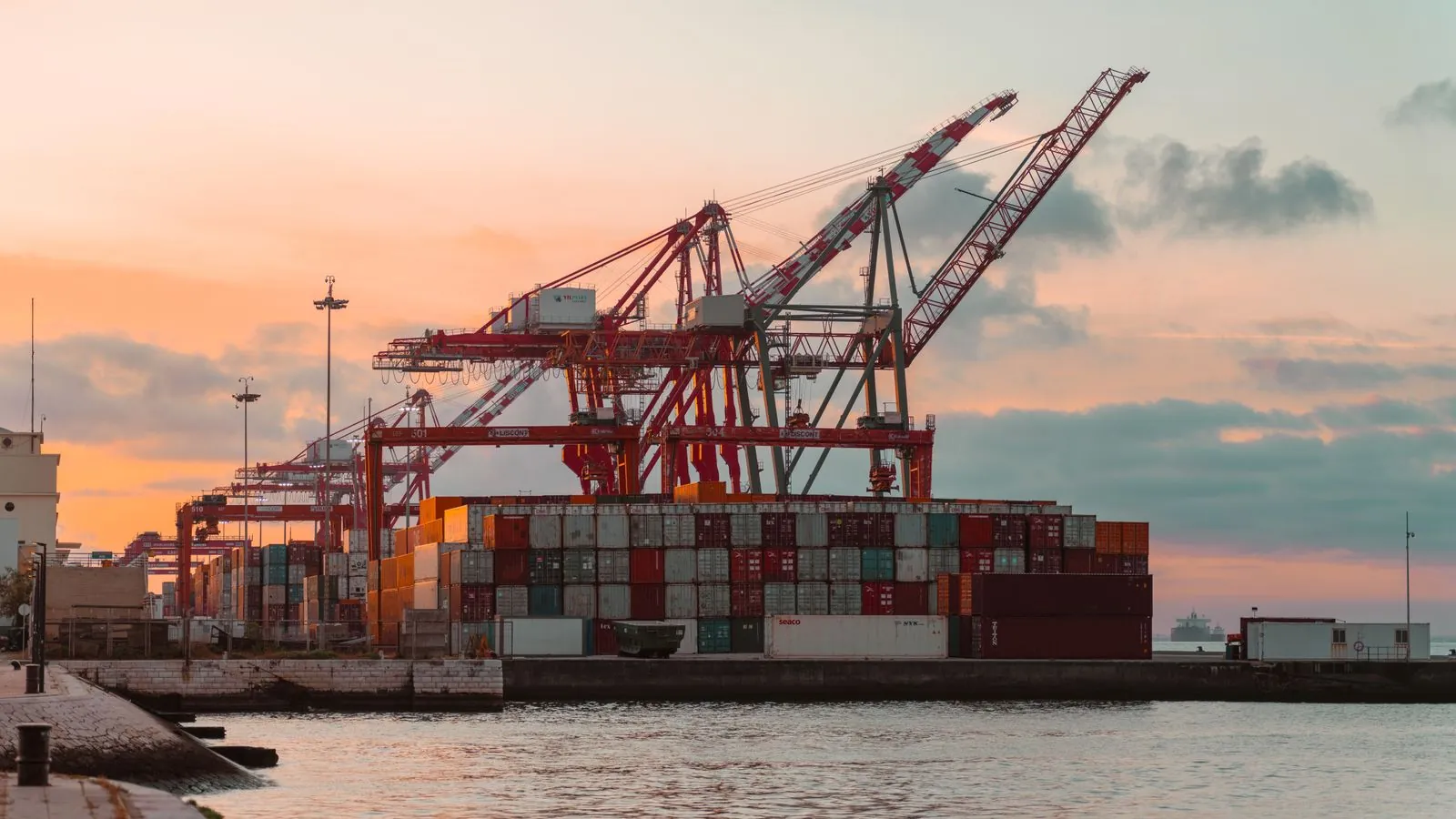 Grúas y contenedores en una terminal portuaria al atardecer, como las del puerto de Caucedo, en Boca Chica