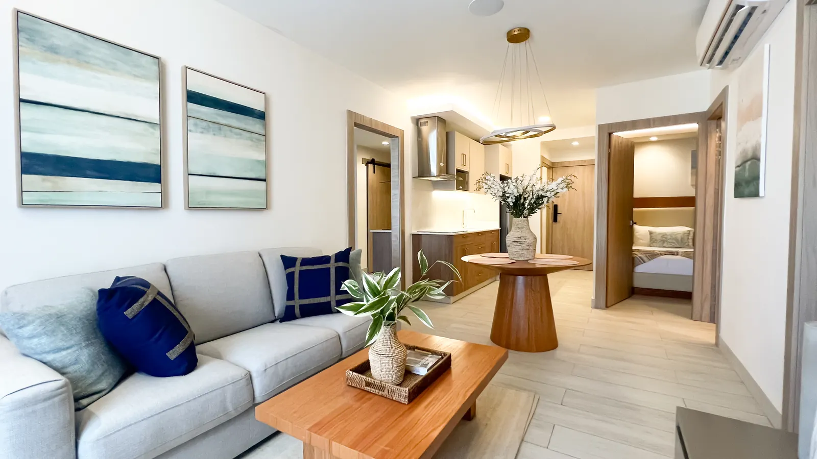 Sala y comedor del apartamento modelo de Cruise On Land Punta Cana, con sofá gris, mesa de madera y cocina al fondo