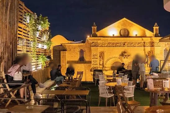 Azotea de SugarCane de noche, con mesas y la Catedral Primada de América iluminada al fondo, Zona Colonial