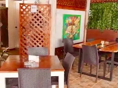 Salón de Trastevere con mesas de madera, sillas de fibra, una celosía y un cuadro de colores