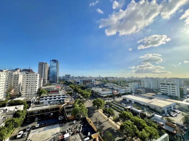Vista desde lo alto de Ensanche Paraíso, con calles arboladas, edificios bajos y torres de apartamentos y oficinas al fondo, en Santo Domingo | Ensanche Paraíso visto desde lo alto: calles arboladas, edificios bajos y, al fondo, las torres de apartamentos y oficinas que van cambiando el perfil del sector.