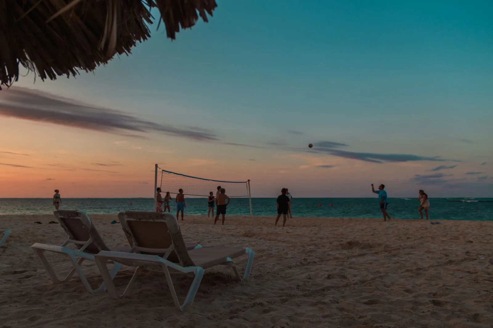 Personas jugando voleibol al atardecer en una playa de Punta Cana, República Dominicana, con tumbonas en primer plano